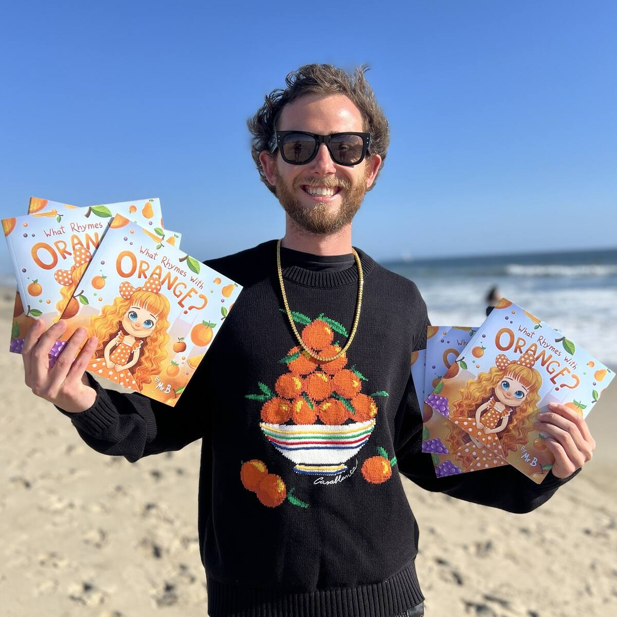 Mr B holding copies of What Rhymes With Orange on the beach